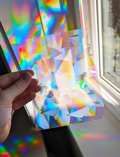 a hand is holding an object in front of a window with colorful light coming through it