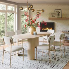 a dining room table with chairs and a fire place in the back ground, surrounded by large windows