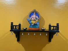 a shelf with an idol on it in front of a yellow wall and hanging bells