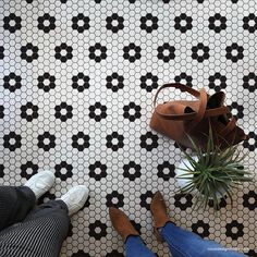 two people standing on a tiled floor next to a potted plant and brown shoes