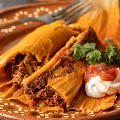 an enchilada with meat, sour cream and salsa on a brown plate