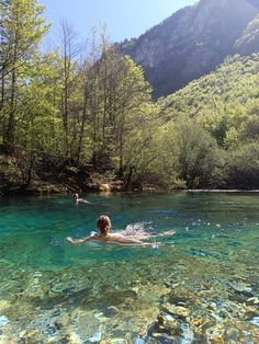 a person swimming in the middle of a river surrounded by trees and mountains on a sunny day