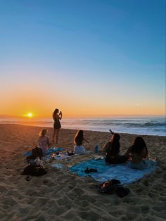 a group of people sitting on top of a beach next to the ocean at sunset