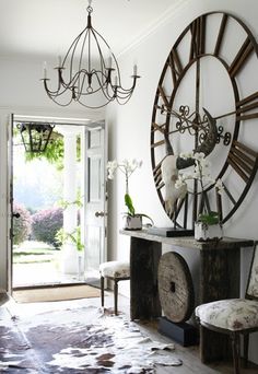 a large clock mounted to the side of a white wall next to a wooden bench