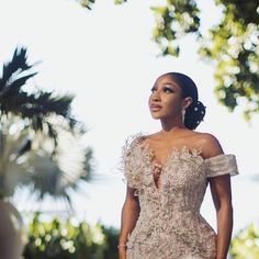 a woman in a wedding dress standing next to a palm tree and looking off into the distance