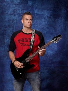 a man holding a black guitar in front of a blue background