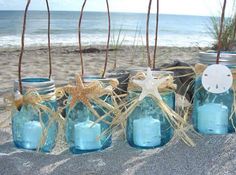 blue mason jars with sand and starfish on the beach next to them, tied in twine