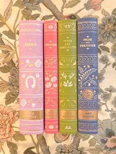 three books sitting on top of each other in front of a flowery wallpaper