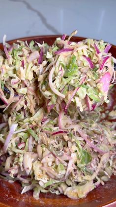 a plate full of coleslaw salad on top of a wooden bowl with tongs