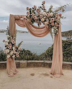 an outdoor wedding setup with flowers and draping on the arch over looking the water