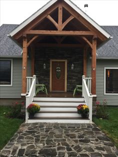 the front porch is covered with wood and has two green chairs on it, along with flowers