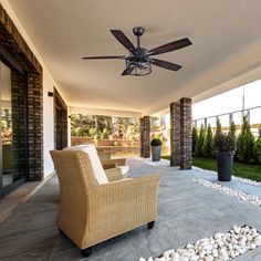 a patio with a couch and ceiling fan on it's side wall, surrounded by rocks