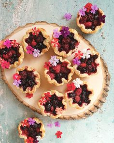 several small pies with flowers on them are sitting on a wooden platter next to petals