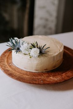 a white frosted cake on a wooden platter with blue and white flowers in the middle