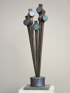 a metal sculpture on top of a white pedestal with four blue flowers in the center