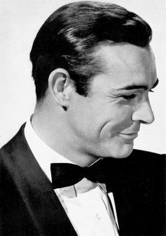 a man in a tuxedo and bow tie looking to his left with a smile on his face