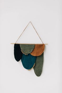 a wall hanging made out of felt and wood with green, blue, brown and black leaves