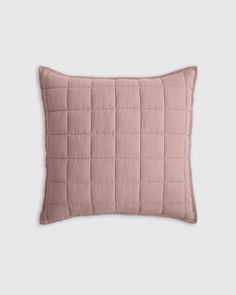 the pink quilted pillow is shown on a white background, it has a square shape and