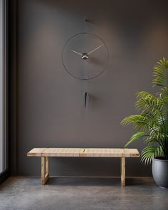 a clock mounted to the side of a wall above a wooden bench next to a potted plant