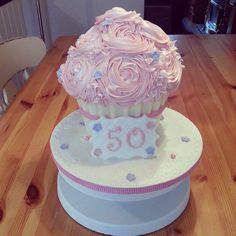 a large cupcake sitting on top of a white cake stand with pink frosting