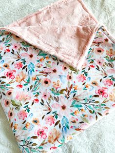 a pink blanket laying on top of a bed next to a white sheet with flowers