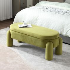 a green foot stool sitting on top of a white rug in front of a bed