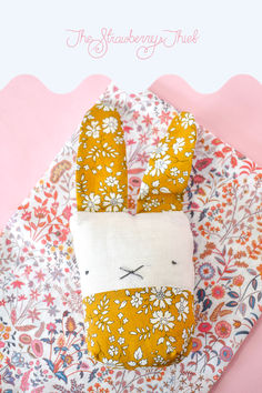 an orange and white bunny pillow sitting on top of a pink tablecloth with flowers