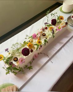 a long cake with flowers on it sitting on a table next to plates and cups