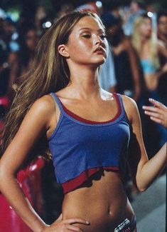 a woman with long hair standing in front of a crowd wearing a blue and red top