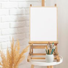 an easel with pencils and pens on it next to a white brick wall