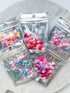 four bags filled with assorted buttons on top of a white table next to each other