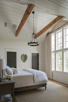 a large bedroom with white walls and wood beams on the ceiling, along with two windows