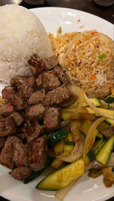 a white plate topped with meat and veggies next to rice on top of a table