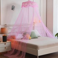 a bed with a pink canopy over it in a room next to a table and lamp