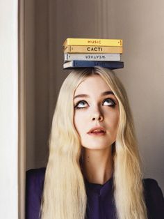 a woman with long blonde hair and two books on her head, smiling at the camera