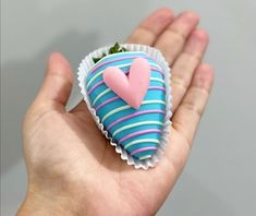 a hand holding a blue and pink heart shaped cake in it's left palm