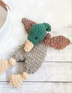 a crocheted stuffed duck laying on top of a white fur covered floor next to a hat