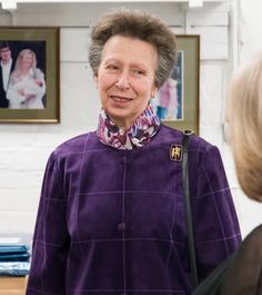 an older woman standing in front of a table talking to another woman who is wearing a purple shirt