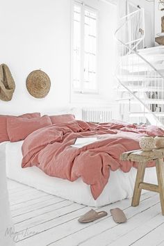 a bed with pink sheets and pillows in a white room next to a spiral staircase