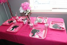 a table set with pink and white polka dot plates, napkins, utensils and flowers