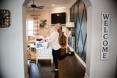 a woman standing in a living room holding a laundry basket and looking up at the ceiling