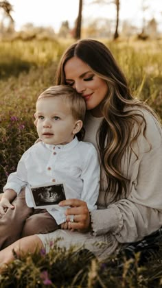 a woman holding a baby while sitting in the grass