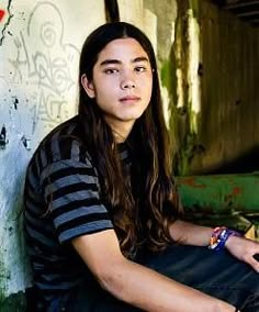 a young man sitting on the ground next to a wall with graffiti all over it