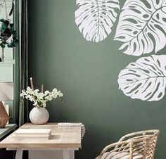 a green wall with white leaves painted on it and a wicker chair in the foreground