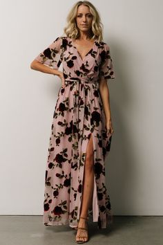 a woman in a pink floral print dress standing against a white wall with her hands on her hips