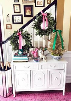 a white dresser topped with wreaths next to a stair case covered in pink and green ribbon