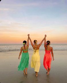 three women are walking on the beach with their arms in the air as the sun sets