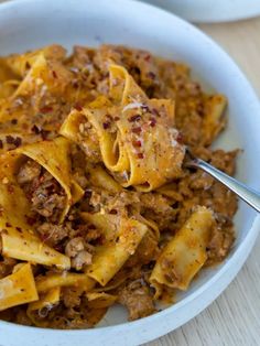 a white bowl filled with pasta covered in meat and sauces on top of a wooden table