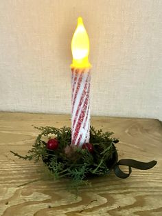 a lit candle sitting on top of a wooden table next to a small bowl filled with greenery