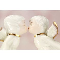 two white angel figurines with gold trimmings kissing each other on a pink background